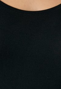 Tessuto nero a coste con una texture liscia e un collo rotondo, che mette in evidenza un primo piano del materiale del capo e dei dettagli delle cuciture.