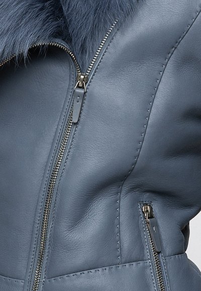 Giacca di pelle blu con colletto in pelliccia sintetica, zip asimmetrica e cuciture dettagliate. Texture liscia con accenti metallici.