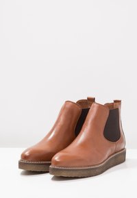 Brown leather ankle boots with black elastic side panels, smooth surface, round toe, and textured sole for grip.