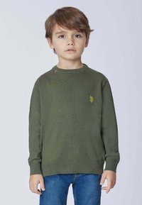 Maglione verde a maglia con collo rotondo, dotato di un piccolo logo giallo e di un accento a contrasto vicino al colletto. Abbinato a jeans blu.