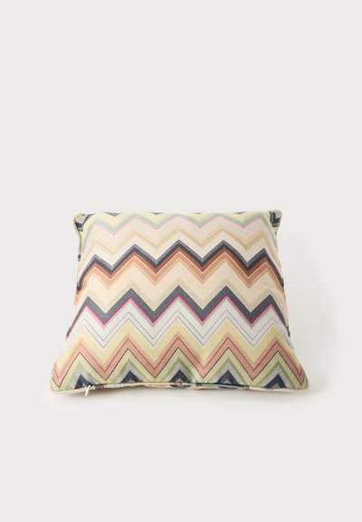 Coussin carré avec motif zigzag multicolore dans des tons beige, rose, vert et bleu sur un fond clair.