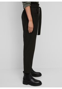 Pantalons noirs fuselés avec une ceinture en tissu, deux poches latérales et une texture lisse, associés à des bottines noires épaisses.
