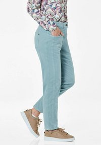 Lichtblauwe stretchbroek met twee zijzakken, slim fit, en subtiele stikdetails. Gecombineerd met beige sneakers.