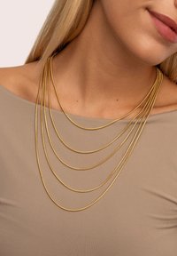 Gelaagde gouden ketting met meerdere strengen, gladde textuur, lichtgewicht ontwerp, elegant vallend over een neutraal gekleurde top.