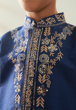 Prenda bordada de color azul marino con intrincados patrones florales dorados y lentejuelas. Presenta un cuello tipo banda y un diseño detallado en el escote.