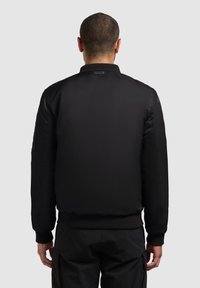 Giubbotto bomber nero con una finitura liscia e lucida. Presenta un colletto e polsini a coste, tasche laterali con zip e una vestibilità rilassata.