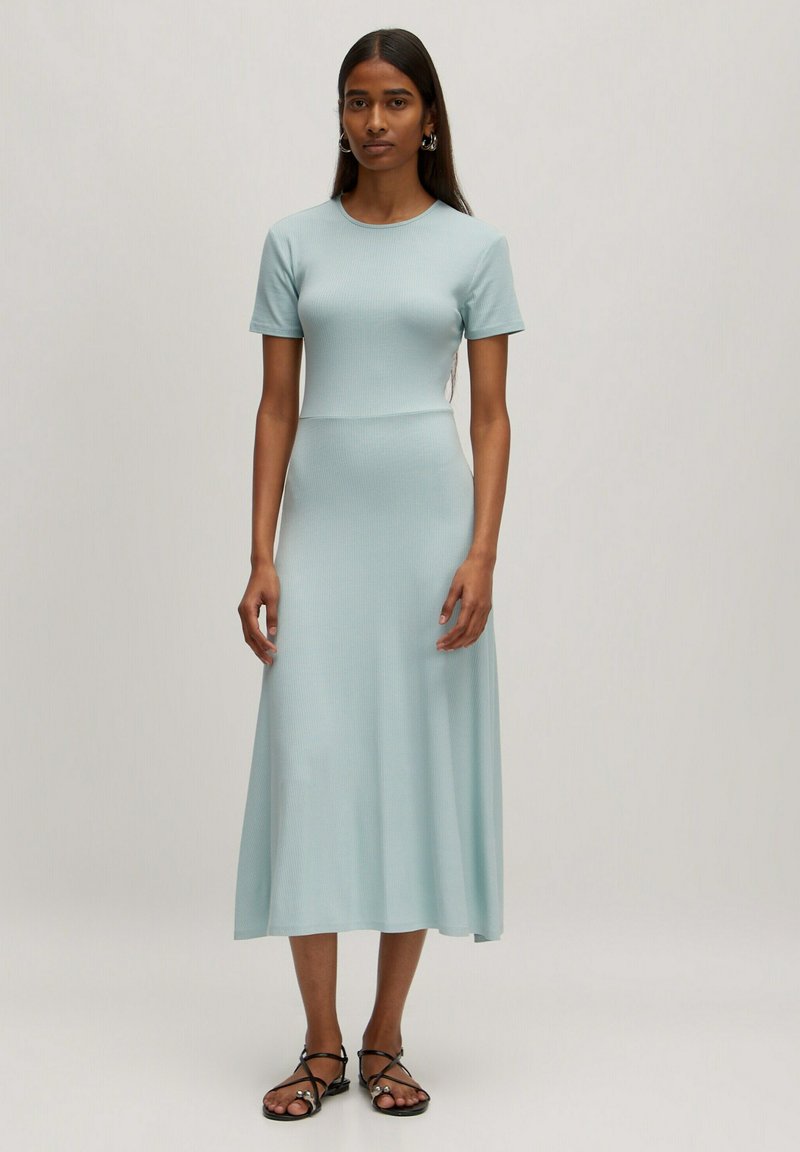 Helles blaues, geripptes Midi-Kleid mit kurzen Ärmeln und rundem Ausschnitt. Das Kleid hat ein figurbetontes Oberteil und einen fließenden Rock. Trägt dazu Riemchensandalen.