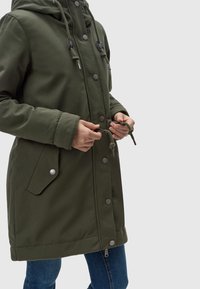 Chaqueta parka color caqui con capucha, tejido texturizado, botones a presión, dos bolsillos laterales y cordones para ajustes.
