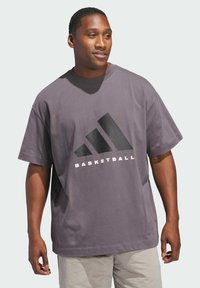 Fialové bavlnené tričko s veľkým čiernym grafickým motívom troch pruhov a slovom "BASKETBALL" bielou farbou pod ním. Krátke rukávy, voľný strih.