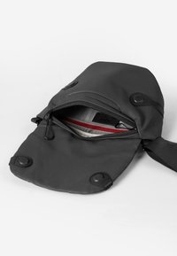 Borsa nera impermeabile a forma arrotondata, con scomparto con zip e chiusure a scatto. L'interno presenta un rivestimento a motivo a griglia con accenti rossi.