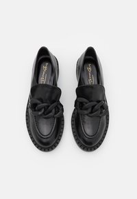 Sorte læder loafers med tyk kædedetalje hen over toppen, rund tå og rillet sål, præsenteret side om side på hvid baggrund.