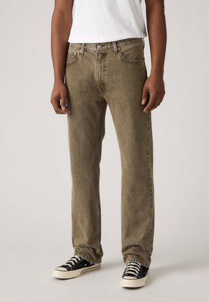 Jeans de denim verde oliva con un corte recto, diseño de cinco bolsillos y cierre de un solo botón, combinados con zapatillas negras y blancas.
