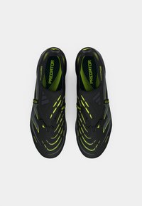 Black athletic shoes with green accents, featuring a smooth texture, streamlined design, and distinctive curved lines across the surface.