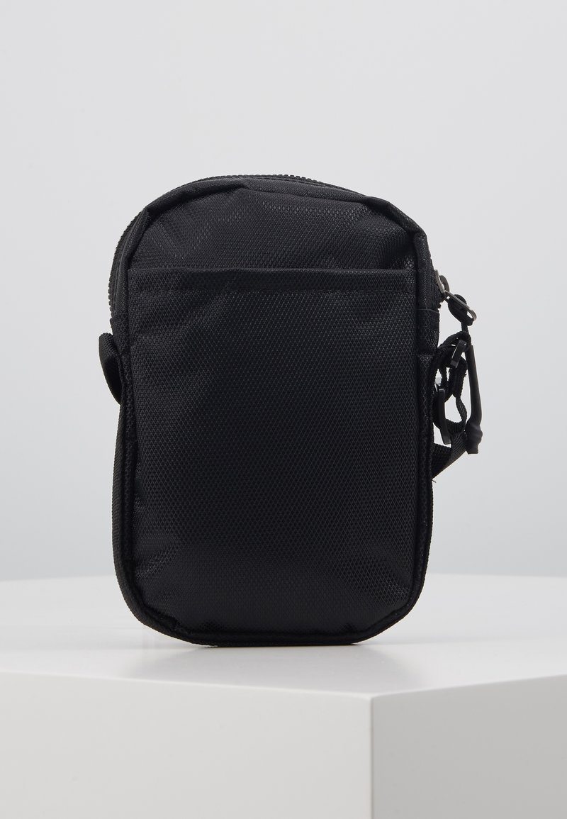 Sac en tissu en maille noire avec fermeture éclair, forme rectangulaire, poche avant et attachement de sangle unique sur le côté.