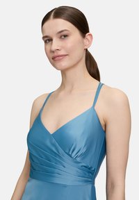 Ein himmelblaues Satin-Kleid mit schmalen Trägern, einem V-Ausschnitt und gerafften Details an der Taille, das eine schlichte Silhouette schafft.