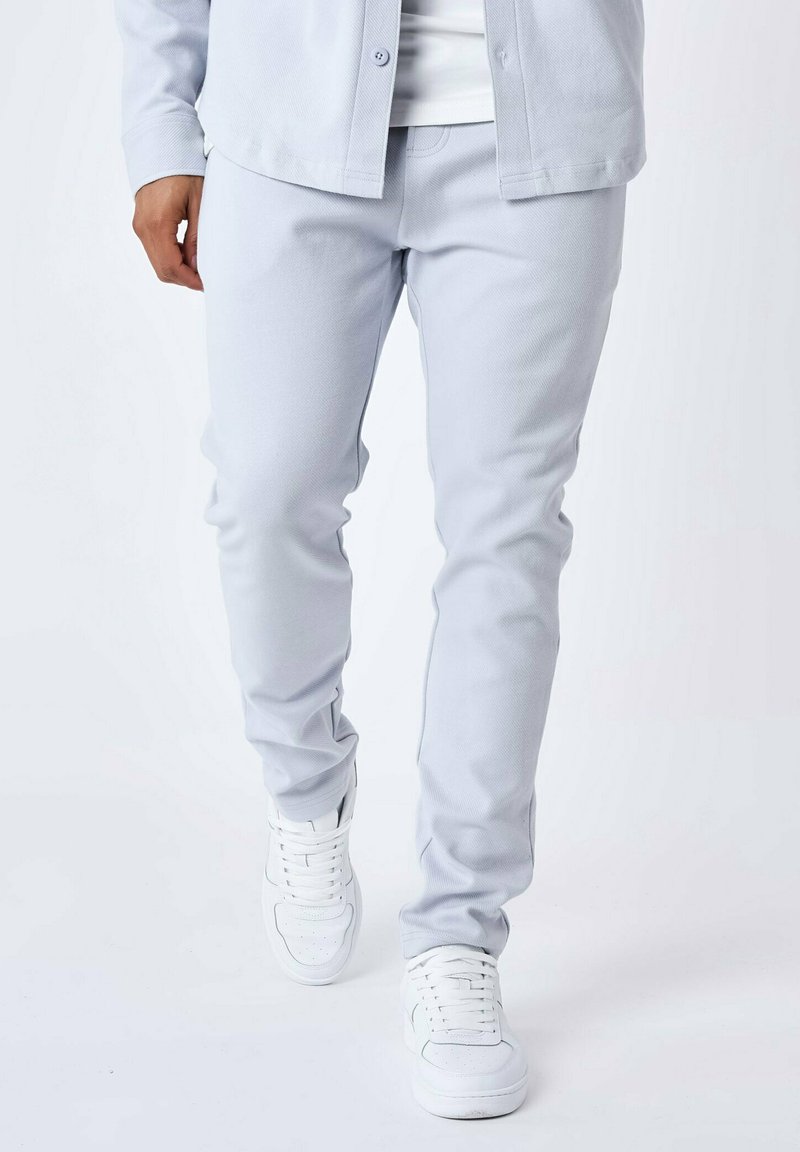 Lys grå bukser med en glat tekstur, slim fit design, parret med hvide sneakers. Synlig syning og en knap-klassisk skjorte.