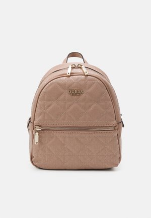 Petit sac à dos beige matelassé avec poche zippée à l'avant, fermetures éclair dorées et logo Guess à l'avant, sur un fond uni.