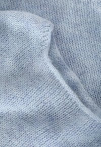 Miękka, jasnoniebieska dzianina z delikatną fakturą, charakteryzująca się luźnym splotem i subtelnymi odcieniami koloru.