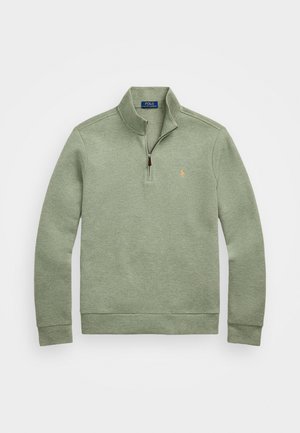 Šviesiai žalias megztinis su puse užtrauktuko, pagamintas iš minkštos medžiagos, su mažu siuvinėtu logotipu ant krūtinės.