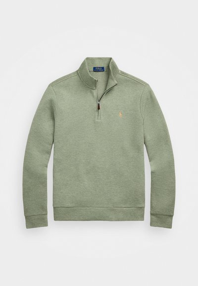 Ljusgrön pullovertröja i mjukt material, med en halv dragkedja i halsen och en liten, broderad logotyp på bröstet.