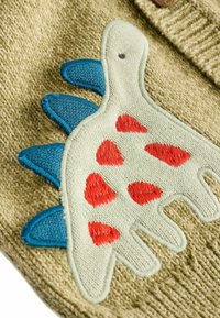 Tissu tricoté vert avec une finition texturée présentant un motif de dinosaure blanc. Le dinosaure a des pointes bleues et des taches rouges.