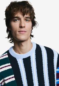 Pruhovaný sveter s rôznymi textúrami; farby zahŕňajú námornícku modrú, zelenú, bielu a svetlomodrú. Okrúhly výstrih a mäkká textília.