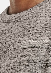 Tessuto grigio con texture e un motivo a macchie. Presenta un logo testuale in bianco. Collo rotondo senza cuciture visibili. Vista ravvicinata.