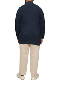 Marineblauwe trui met textuur en ruitpatroon, lange mouwen en geribde manchetten, gecombineerd met lichtbeige corduroy broek en sneakers.