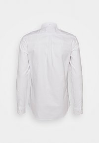 Bílá košile s dlouhým rukávem, zobrazená zezadu, s zapnutými manžetami a střední záhybem na zádech pod límečkem.