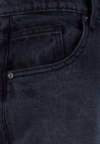 Dark denim jeans featuring a pocket with contrast stitching and a metal button detail. The fabric has a slight sheen and rough texture.