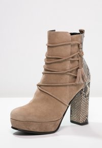 Stivaletti alla caviglia in suede beige con lacci avvolgenti, dettaglio con nappine e tacco a blocco in pelle di serpente con motivo a scaglie.