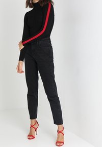 Černý top s dlouhým rukávem s červenými pruhy po stranách a černé džíny s vysokým pasem. Outfit doplňují červené sandály na podpatku s pásky. Hladké, přiléhavé materiály.