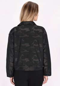 Sort camouflagejakke med en afslappet pasform, der har en krave, lange ærmer og knapmanchetter, lavet af et glat, let materiale.