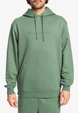 Grön hoodie med en känguruficka, justerbara snören och diskret logotyp på bröstet. Tillverkad av mjukt, texturerat tyg.