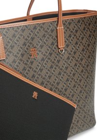 Καφέ τσάντα tote με σχέδια, δερμάτινες λαβές και μια ταιριαστή μαύρη θήκη, και οι δύο με μικρές χρυσές διακοσμητικές λεπτομέρειες λογότυπου.