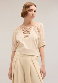 Lichtbeige blouse met een gestructureerd haakontwerp bij de halslijn, korte pofmouwen en een relaxte pasvorm. Gecombineerd met bijpassende broek.