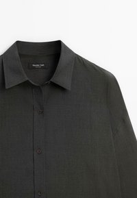 Camicia button-up grigio scuro realizzata in tessuto testurizzato, con colletto classico e una leggera lucentezza, orlo arrotondato e una tasca frontale singola.