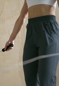 Grijze sportbroek met een elastische tailleband, die een gladde textuur benadrukt, gecombineerd met een zwart springtouwhandvat op een neutrale achtergrond.