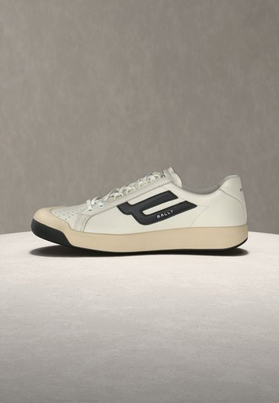 Baskets blanches basses avec embout de semelle noir, logo noir et inscription "BALLY" sur le côté, semelle intermédiaire beige et lacets blancs sur fond uni.
