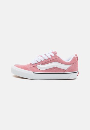 Las zapatillas de ante rosa cuentan con cordones blancos, una franja de cuero blanco y una suela negra. Tienen una puntera redonda y perforaciones mínimas para ventilación.