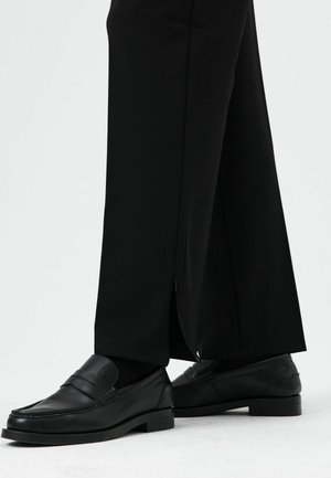 Zwarte wijde broek met zijrits en strakke zwarte loafers met een gestructureerde afwerking en verhoogde banddetail.
