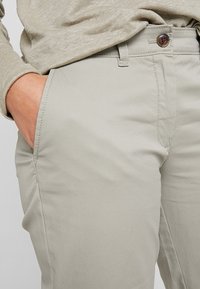 Lichtgrijze katoenen broek met een rechte pasvorm, zijzakken en een knoopsluiting. Soepele textuur, minimale detailing, veelzijdig ontwerp.