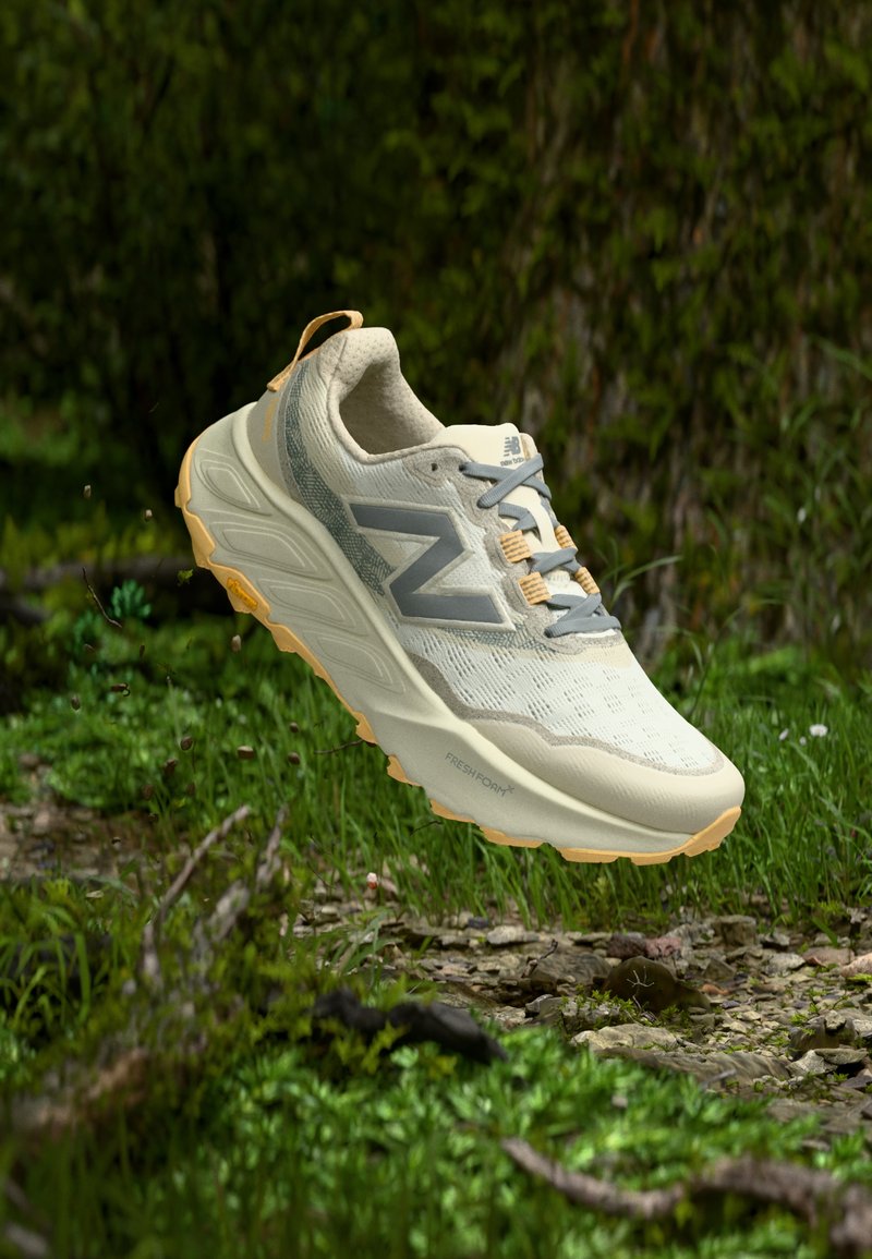 Ανοιχτό μπεζ αθλητικό παπούτσι με γκρι λεπτομέρειες, επάνω μέρος από πλέγμα, μαξιλαρωμένη σόλα και χαρακτηριστικό μοτίβο πρόσφυσης στην εξωτερική σόλα, σχεδιασμένο για άνεση.