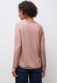Hellrosa Langarmoberteil mit rundem Ausschnitt und weicher Textur. Der Rücken hat einen leicht abgerundeten Saum und wird mit dunkelblauen Jeans kombiniert.