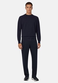 Jūras spēku zilo adījuma džemperi ar apaļu kaklu un raglāna piedurknēm, saskaņoti ar atbilstošām šaurām biksēm. Gluda tekstūra un plūdena forma.