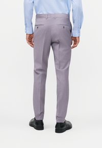 Άνδρας που φοράει κομψό ανοιχτό γκρι παντελόνι, μαύρα παπούτσια και ανοιχτό μπλε πουκάμισο με μακριά μανίκια, φαίνεται από πίσω.