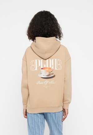 Beige Kapuzenpullover mit einem großen Grafikmotiv einer Kaffeetasse und Untertasse auf dem Rücken. Das Design zeigt "PGDB" über dem Bild und den Text "Peace Of Mind" darunter.