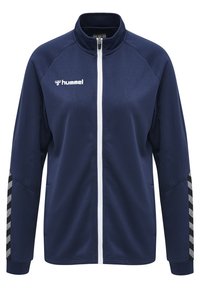 Marineblauwe jas van een gestructureerde stof. Heeft een hoge kraag, volledige ritssluiting, witte accenten en zwart-witte strepen op de mouwen.