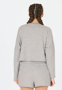 Grijze cropped longsleeve shirt gecombineerd met bijpassende shorts. Zachte textuur, eenvoudig ontwerp en een relaxte pasvorm. Geen opvallende patronen of accenten.