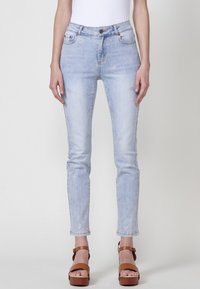 Jeans de denim azul claro con corte slim, adornados con embellishments plateados en forma de estrella. Presentan un clásico diseño de cinco bolsillos y cierre de botón.